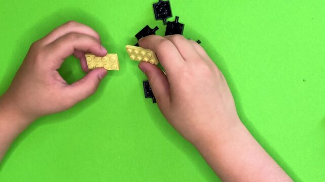 A close-up of children's hands building something out of building blocks against a bright green background. Horizontal video