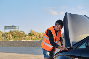 Man in safety vest inspecting broken down car engine