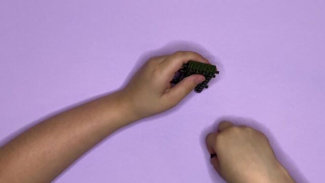Close-up of children's hands building something out of building blocks on a bright purple background. Horizontal video