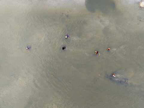 Aerial view of people working in the muddy river where the water reflects the sky, creating a serene yet industrious scene, Tetulia, Rangpur Division, Bangladesh.