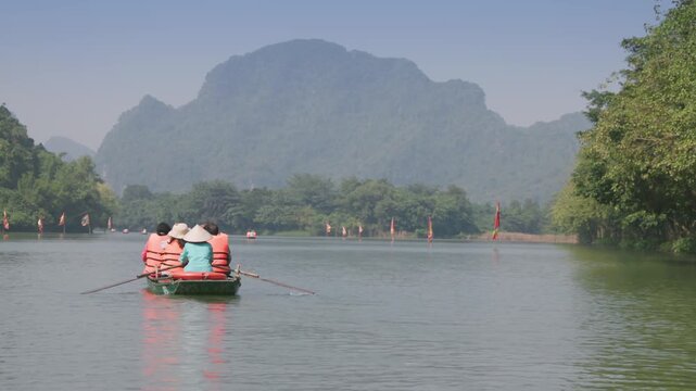 Tourists wearing life vests enjoy a boat ride on the River in Ninh Binh, Vietnam. They are experiencing the natural beauty of the region and local culture.