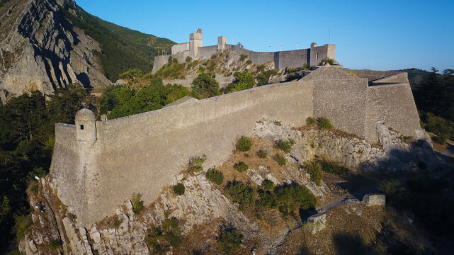Aerial view of the formidable Citadelle de Sisteron stands proudly atop a rocky crag, its ancient stone walls bathed in the warm glow of the sun, Sisteron, Provence-Alpes-Cote d'Azur, France.