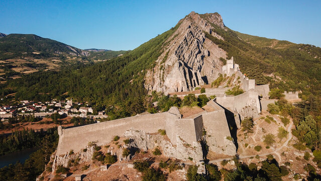 Aerial view of the imposing Citadel of Sisteron fortress clinging to the craggy mountainside, a testament to history amidst the lush landscape, Sisteron, Provence-Alpes-Cote d'Azur, France.