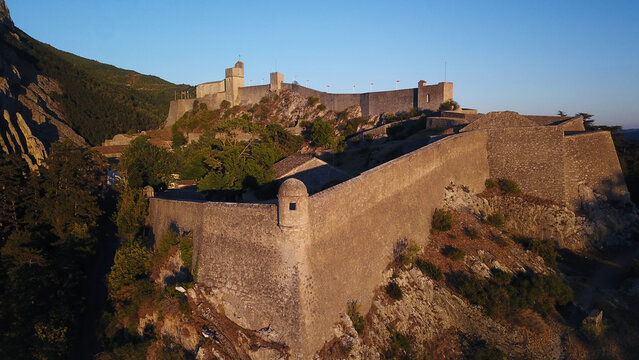 Aerial view of the ancient Citadel standing proudly atop the hill, its stone walls glowing warmly in the golden light of dusk, Sisteron, Provence-Alpes-Cote d'Azur, France.