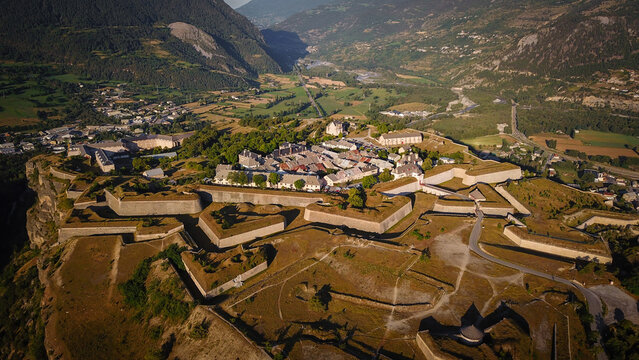Aerial view of the fortified city walls and bastions, atop a hill, against a backdrop of verdant valleys and distant mountains, Mont-Dauphin, Provence-Alpes-Cote d'Azur, France.
