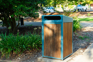 Public park rubbish bin with wood panel design in landscaped urban garden