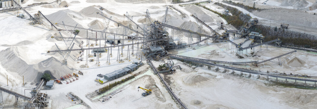 Aerial view of a vast, stark white quarry landscape carved by heavy machinery and conveyor belts against a backdrop of mineral piles, Miami, Florida, United States.