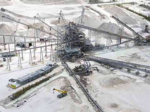 Aerial view of a vast limestone quarry with heavy machinery amidst pale dunes under the sun, a landscape of industry, Miami, Florida, United States.