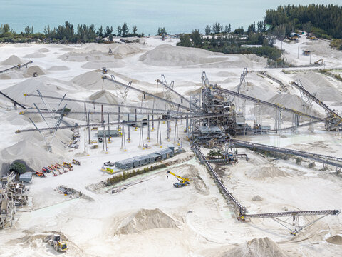 Aerial view of a sprawling limestone quarry where pristine white mounds meet the industrial machinery under a pale sky, Miami, Florida, United States.