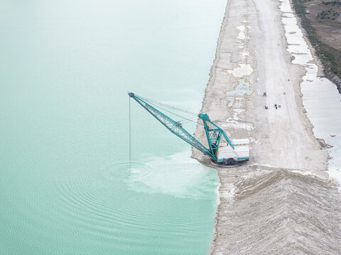 Aerial view of a colossal crane poised at the water's edge, its turquoise body a stark contrast against the pale, sandy shore and the milky aquamarine water, Miami, Florida, United States.