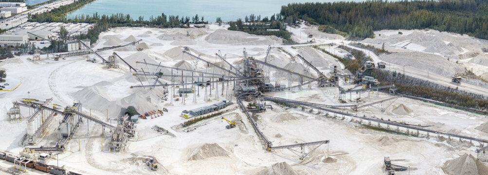 Aerial view of an expansive limestone quarry, where stark white mounds meet the dark green of distant trees under a pale sky, Miami, Florida, United States.