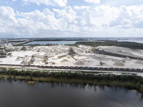 Aerial view of the stark white quarry contrasting against the dark water and green vegetation under a vast sky, Limestone Quarry, Miami, Florida, United States.