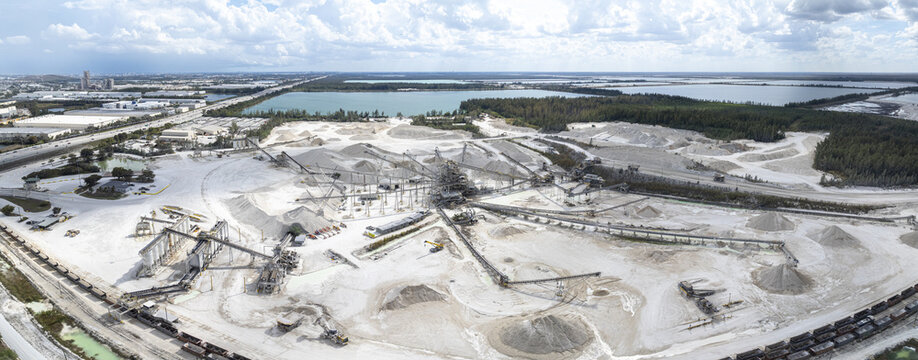 Aerial view of a vast limestone quarry with stark white piles contrasting against a backdrop of lush green trees and a tranquil blue lake, Miami, Florida, United States.