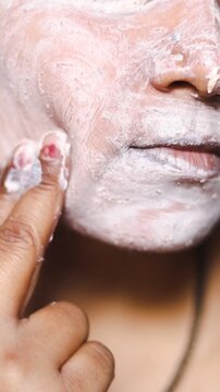 Young Indian woman applying face scrub and gently massaging her skin for exfoliation and deep cleansing at home.