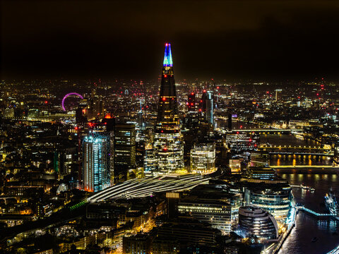 Aerial view of The Shard piercing the night sky amidst a tapestry of city lights, with the London Eye subtly glowing in the distance, London, Greater London, United Kingdom.