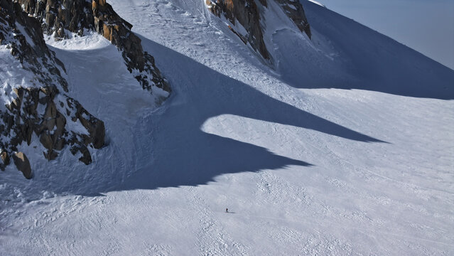 Aerial view of stark white snowfields contrasted by jagged, dark rock formations, a solitary figure standing in the expanse, Vallee Blanche, Chamonix, Auvergne-Rhone-Alpes, France.