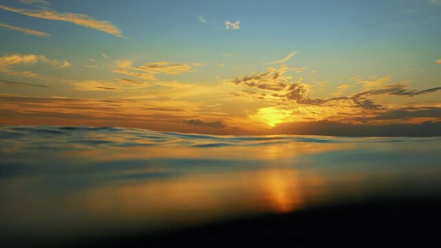 Slow Motion ocean surface from underwater at sunset with rays of light. Crystal clear breaking ocean wave with waving waterline. Sunrise over calm sea. Dawn over horizon, ocean, water - timelapse