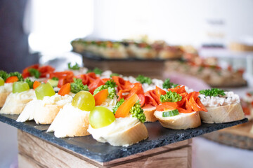 Assorted open-faced sandwiches and canapés with fresh vegetables, cheese, grapes and salami, beautifully arranged on a catering buffet table.	
