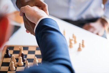Fototapeta na wymiar Close-up of a handshake over a chessboard, symbolizing agreement or partnership. Chess pieces visible, indicating a strategic or competitive context. Business people in a meeting.