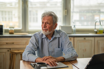 Senior man concentrating on paperwork and digital tablet at home table