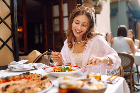 A happy woman eats fresh Italian pasta at a cafe table. A young tourist enjoys spaghetti on a sunny day on the terrace. Concept of food, enjoyment.