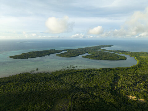 Aerial view of a lush green island surrounded by turquoise waters and distant clouds, Karimunjawa, Central Java, Indonesia.
