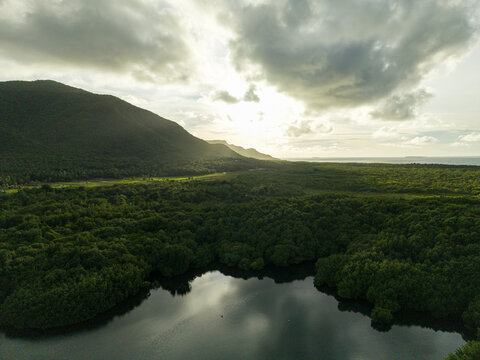 Aerial view of sunlight filtering through the clouds over lush mangrove forests and calm waters, Karimunjawa, Central Java, Indonesia.