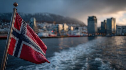 Fototapeta premium View of a Norwegian flag waving on a boat near buildings and mountains in Bergen during sunset or twilight hours