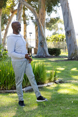 Senior African American man standing in park wearing hoodie holding phone and keys, copy space