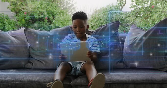 Child adjusting and raising white tablet on couch, blue overlay aligning with screen for learning