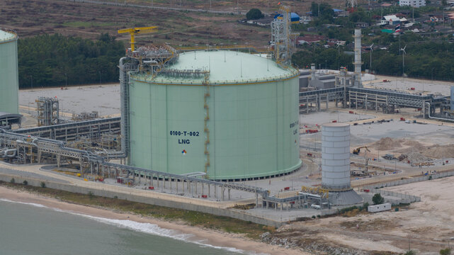Aerial view of an industrial complex with large LNG tanks juxtaposed against the soft shoreline, a symphony of steel and sand, Map Ta Phut, Rayong, Thailand.
