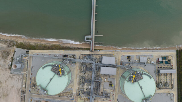 Aerial view of the LNG terminal tanks meet the sea with a long pier stretching out, where the industrial complex meets the natural shore, Map Ta Phut, Rayong, Thailand.