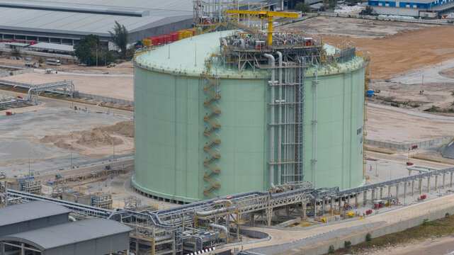 Aerial view of a colossal, light green LNG tank, encircled by metallic structures and pathways, standing prominently against the industrial landscape, Map Ta Phut, Rayong, Thailand.