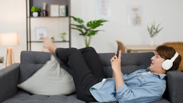 Asian Man Relaxing on Sofa Listening to Music with Headphones