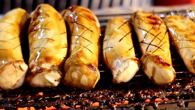 Authentic Thai street food cooking featuring healthy grilled mushrooms. Watch the sauce glisten on the meaty stems as they slow cook over hot coals for an evening market experience.