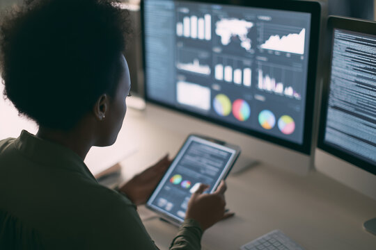 Woman sitting at multiple monitors working late night in office, analyzing stock charts and trading financial markets