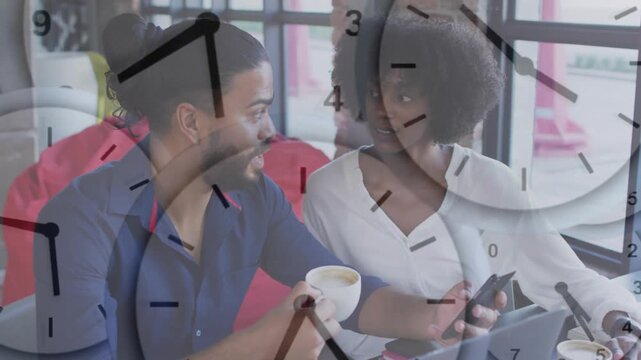 Woman tapping phone, showing man in cafe, clock-face advancing while both discussing work on laptop