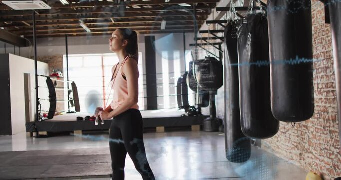 Preparing boxer in pink top, leggings, camera pulling back, adjusting by heavy bags, holding bottle