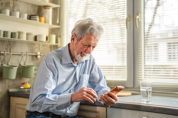 Senior man smiling using smart phone in kitchen