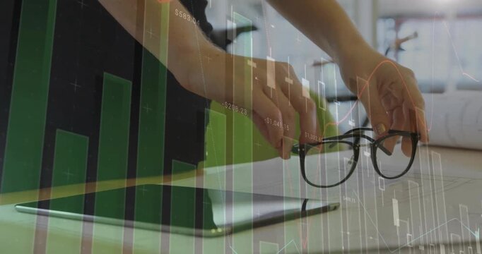 Reaching woman in dark top lifting glasses tapping tablet at office desk with green chart overlay