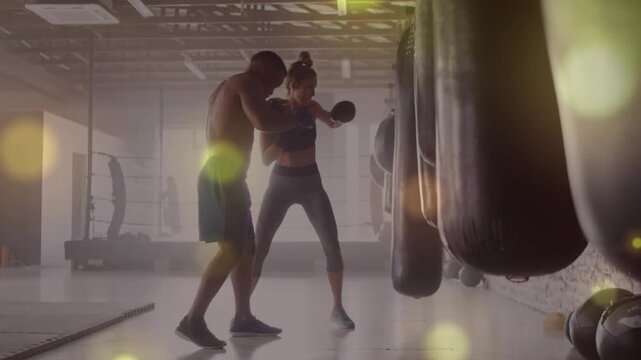 Vertical video: Coach shirtless adjusting guard, trainee punching bags in studio, improving form