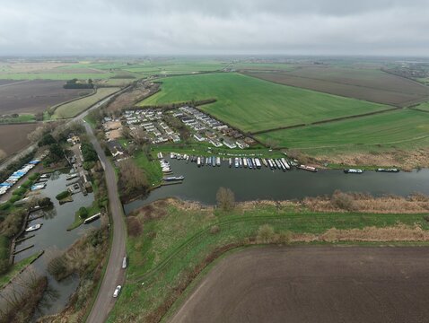 Aerial view of boats nestled in Stretham Ferry Marina's embrace, framed by the lush, agricultural tapestry of the Fens, Ely, United Kingdom.