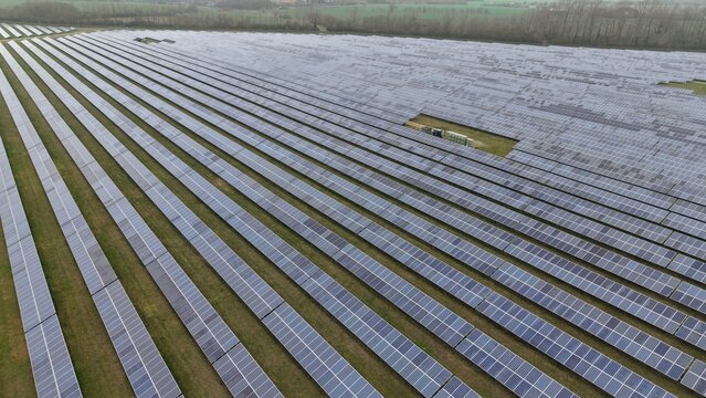 Aerial view of endless rows of solar panels gleam under the pale sky near the former RAF Alconbury, Huntingdon, Cambridgeshire, United Kingdom.