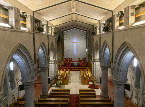 Aerial view of the cathedral interior with arches leading to rows of wooden pews and a radiant blue cross illuminating the altar, Nelson, Nelson Region, New Zealand.