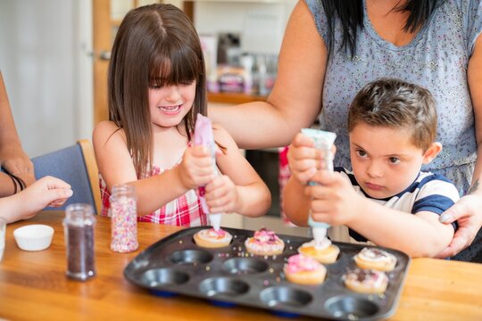 Children decorating cupcakes with icing and sprinkles. Focused kids enjoying cupcake decorating. Fun activity with icing and sprinkles on cupcakes. Kids baking together at home.
