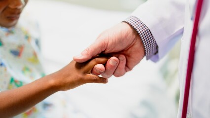 A comforting scene of a doctor holding a child's hand. The doctor offers support, care, and reassurance. The child's hand is gently held by the doctor. Hospital, medical, and healthcare concept.