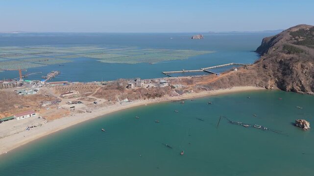 Panoramic aerial video showing large-scale marine aquaculture fields arranged in geometric grid patterns across calm coastal waters near Dalian on the Bohai Sea. 