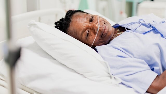 A person lying in a hospital bed, wearing a nasal cannula, smiling gently. The setting is a medical environment, conveying a sense of care and recovery. Hospital, medical, and healthcare concept.