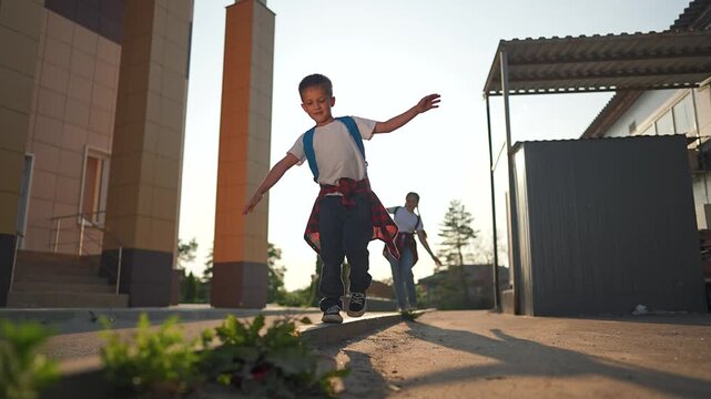 Student boy wearing backpack walks along school building in morning light. Confident child steps with purpose as backpack moves. School path begins with backpack student walk toward knowledge