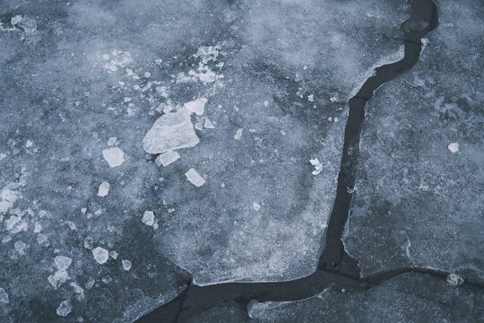 Close up view of a frozen surface featuring icy cracks and broken pieces of ice, reflecting a cold winter day.
